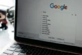 An angled close-up of a open MacBook Air displaying the Google homepage on its screen. The search bar shows "Pexels" typed in, with a dropdown menu displaying search suggestions like "pexels video" and "pexels free photos".