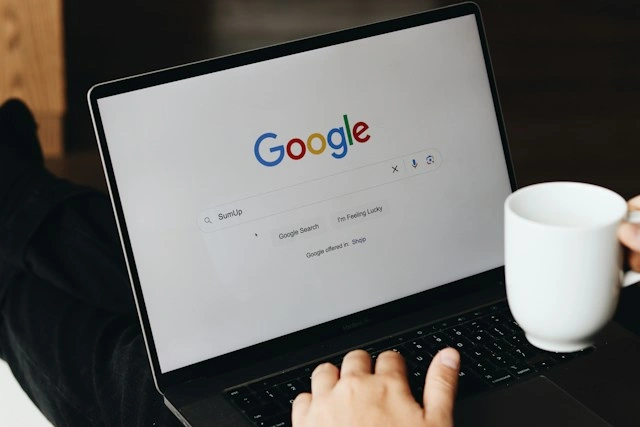 Close-up of a person using a laptop with the Google search engine open, searching for "SumUp", while holding a white mug.